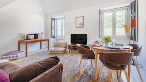 A living room with a sofa, a coffee table, a TV, a fireplace, and a dining area with chairs and a table set for two. - Atelier by the Sea (Porto)