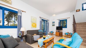 A modern living room with a sofa, armchair, and a coffee table. There is a TV and a staircase in the background. - Villa Rotiana - Three Bedroom Villa, Sleeps 6 (Poli Crysochous)