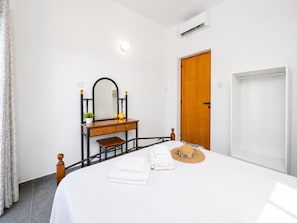 A bedroom with a bed, a wooden dresser with a mirror, a door, and a window.