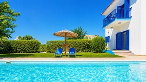 A clear swimming pool with blue chairs and a sun umbrella, surrounded by greenery and a white building with blue accents. - Villa Rotiana - Three Bedroom Villa, Sleeps 6 (Poli Crysochous)