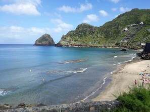A coastal beach with clear waters, rocky outcrops, and a hillside with buildings. - Casa dos Magalhães (Vila do Porto)