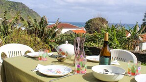 A table set for a meal with a view of the ocean and hills. - Casa dos Magalhães (Vila do Porto)