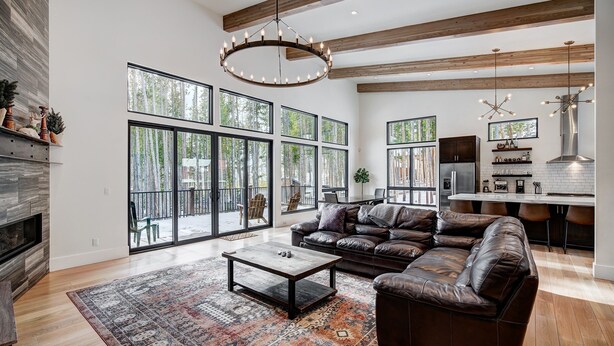 A spacious living room with a large sectional sofa, a coffee table, and a fireplace. There are large windows providing natural light and views of the outdoors.
