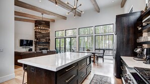 A modern kitchen with a large island, wooden beams, large windows, and a built-in stove.