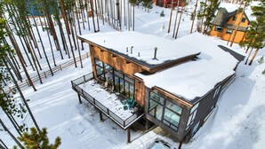 A modern two-story house with a wooden exterior, large windows, and a balcony with outdoor seating.