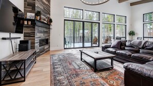A modern living room with a fireplace, large windows, a leather sofa, and a TV.