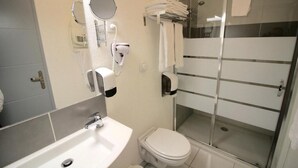 A bathroom with a sink, toilet, and a glass-enclosed shower area. - Hôtel le 15 (Coulounieix-Chamiers)