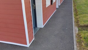 A row of red and white buildings with open doors, a covered walkway, and a grassy area. - Hôtel le 15 (Coulounieix-Chamiers)