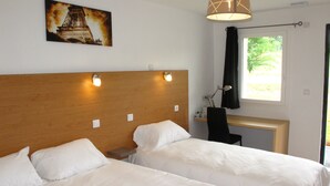 A hotel room with two beds, a wooden headboard, bedside lamps, a desk with a chair, a window with curtains, and a picture of the Eiffel Tower on the wall. - Hôtel le 15 (Coulounieix-Chamiers)