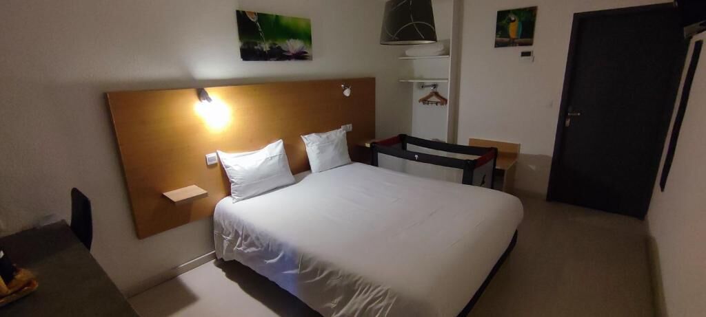 A hotel room with a bed, a bedside table, a lamp, and a door.