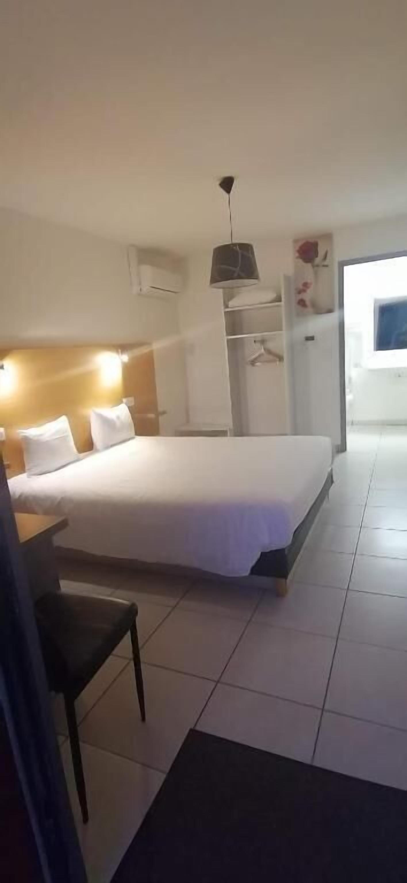 A hotel room with a large bed, a desk, a chair, a wardrobe, and a hanging light fixture.