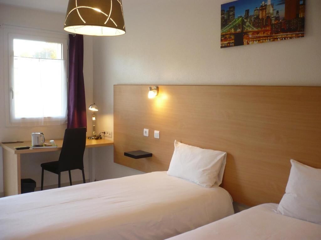 A hotel room with two beds, a desk, a chair, a lamp, and a painting on the wall.
