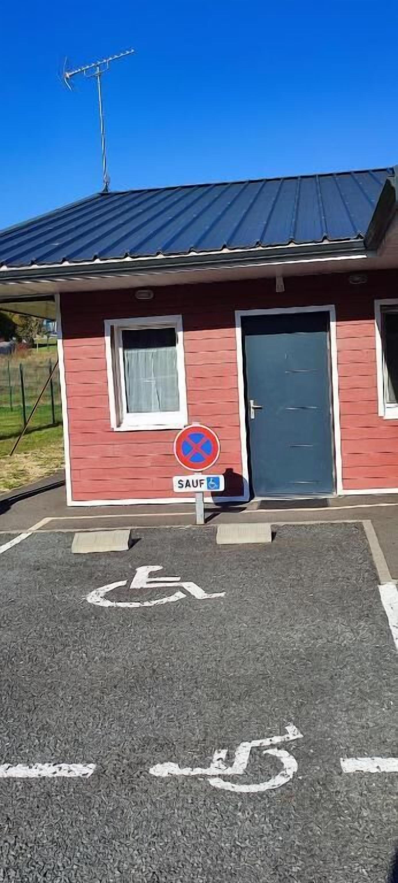Un bâtiment rouge avec une porte bleue, un panneau indiquant qu’il est interdit de se garer et une place de stationnement réservée aux personnes handicapées.