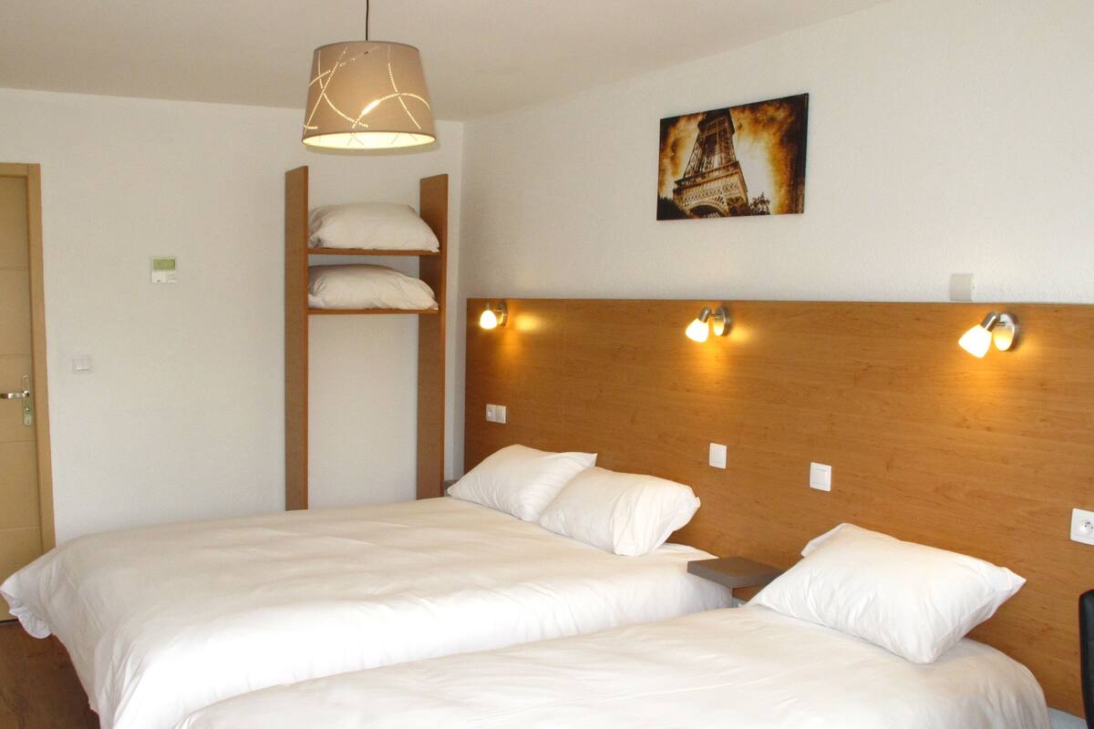 A hotel room with two beds, a wooden headboard, a hanging lamp, and a picture of the Eiffel Tower on the wall.