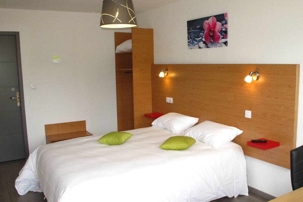 A hotel room with a bed, two pillows, a nightstand, a lamp, a picture on the wall, and a door.