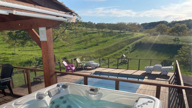 Un bain à remous sur une terrasse en bois, avec vue sur un champ verdoyant et des arbres.