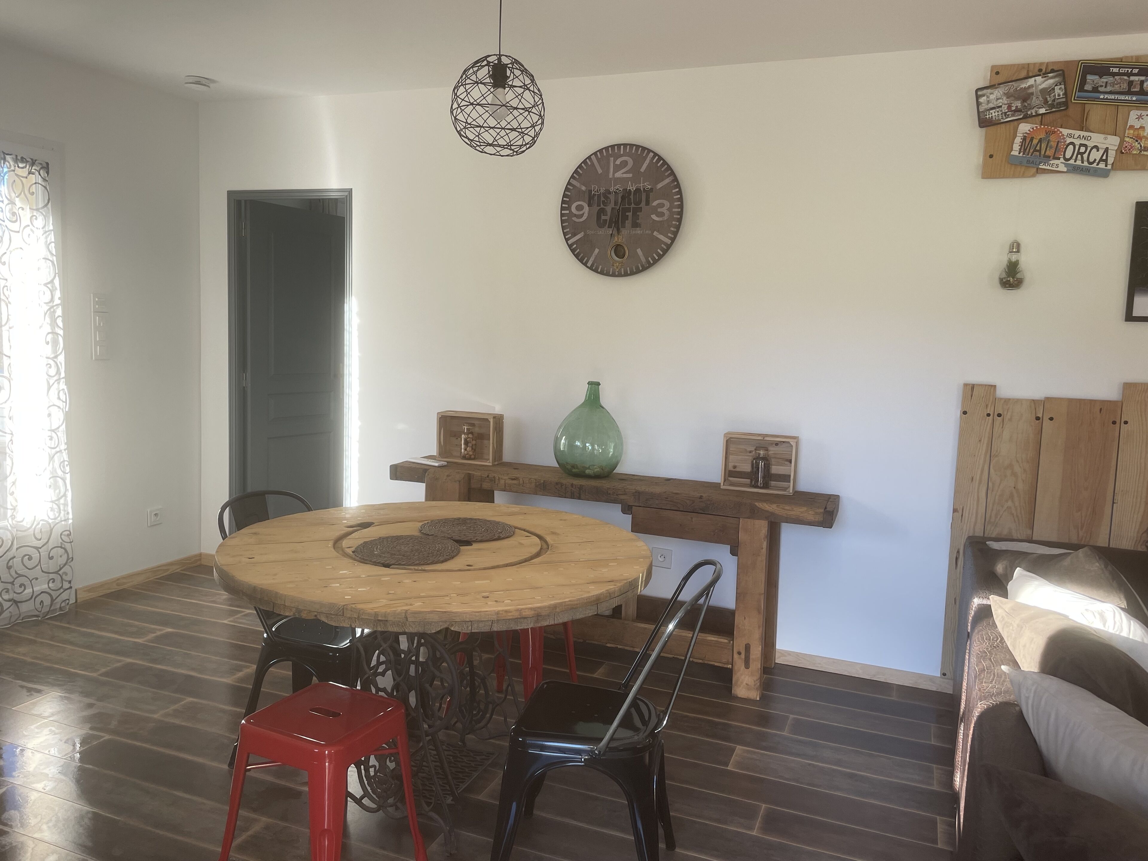 A dining area with a round wooden table, two chairs, a green vase, and a wall clock.