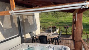 Un bain à remous avec jets, une terrasse en bois, une table avec des chaises et une vue sur un champ verdoyant.