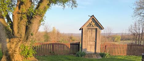 A rustic outdoor setting with a wooden fire pit, picnic tables, and a small wooden structure.