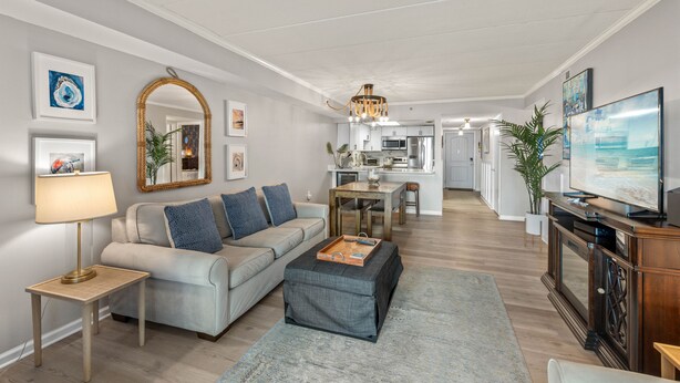 Una sala de estar moderna con sofá, reposapiés y mesa de centro, un comedor con mesa y sillas, y una cocina al fondo.