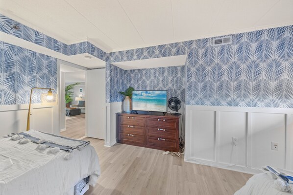 A bedroom with a bed, a dresser, a television, and a fan.