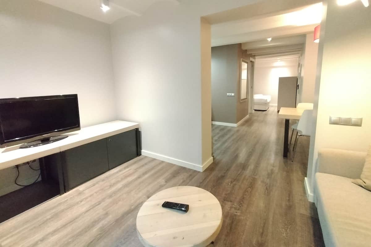 A modern hotel room with a flat-screen TV, a round coffee table, a sofa, and a dining area with a table and chairs.