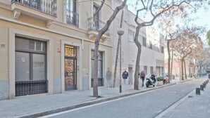 Vista de la calle con un edificio que tiene una puerta metálica grande, una acera y algunas personas caminando.