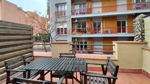 Un edificio de varios pisos con balcones, una banca de madera y una mesa.