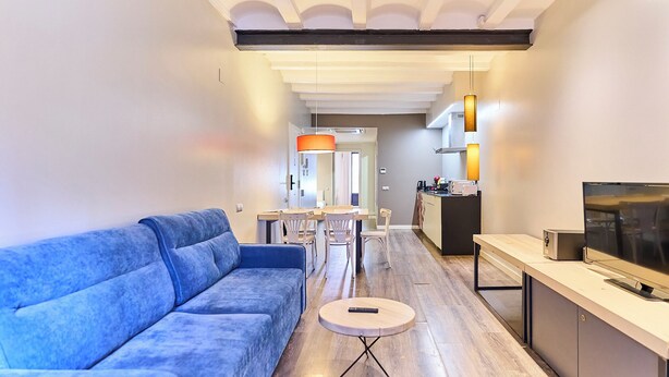 Una sala de estar moderna con un sofá azul, una mesita redonda y un televisor sobre un mueble.