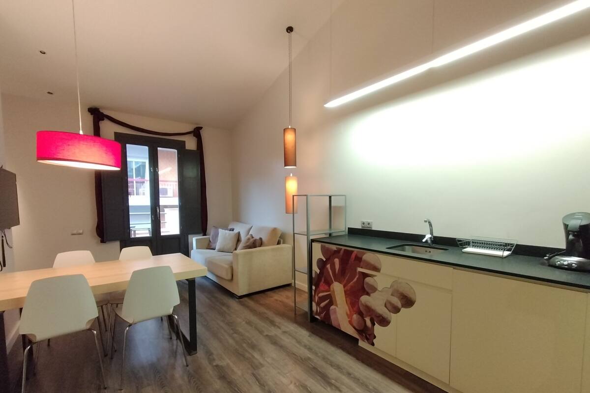 A modern kitchen with a black countertop, a sink, and a coffee maker. There is a dining area with a white table and chairs.