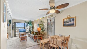 A spacious living area with a wooden dining table, chairs, and a ceiling fan. There is a sofa and a coffee table with decorative items. - Westward Ho 410 by Seaside Vacations & Sales (Ocean City)