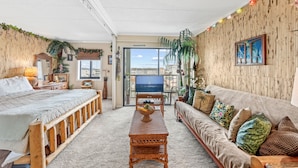 A room with a bed, a sofa, a wooden table, and a television. - Westward Ho 410 by Seaside Vacations & Sales (Ocean City)