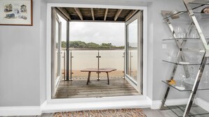 A room with a wooden deck, a table, and a glass display unit. - The Old Pilot Hut, Felixstowe Ferry, Amazing Views (Felixstowe Ferry)