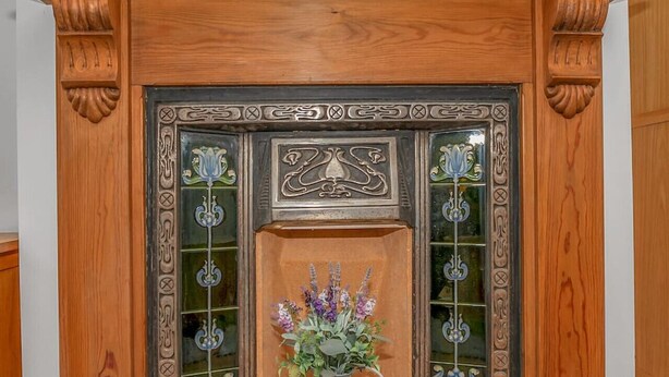 A fireplace with intricate metalwork and a vase of flowers.