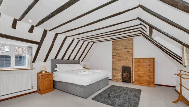 A bedroom with a sloped ceiling, a bed, a dresser, a radiator, and a window with curtains. - Charming Cottage in Barton Mills (Barton Mills)