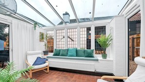 A conservatory with a white bench, green cushions, and potted plants. - Charming Cottage in Barton Mills (Barton Mills)