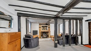 A modern living room with exposed beams, a fireplace, and a wooden cabinet. - Charming Cottage in Barton Mills (Barton Mills)