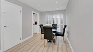 Un espace repas moderne avec une table et des chaises, une porte blanche et une fenêtre avec des stores.