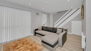 Un salon moderne avec un canapé d’angle, un tapis moelleux et un escalier menant à un autre niveau.
