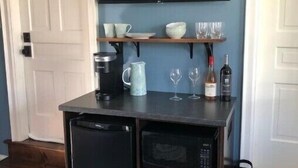 Une cuisine compacte équipée d’un four à micro-ondes encastré, d’une machine à café et d’un petit réfrigérateur. Une étagère au-dessus du plan de travail permet de ranger les tasses et les verres.