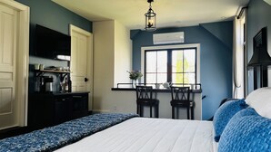 Un dormitorio con cama, ventana con vistas, zona de cocina con cafetera y televisor en la pared.