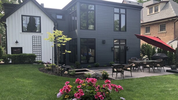Una casa moderna de dos pisos con un patio amoblado, incluyendo mobiliario exterior y un paraguas rojo.
