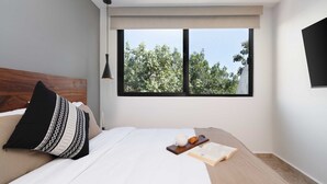 A modern bedroom with a large window, a wooden headboard, and a bedside table with a book and a cup. - 2 BD w/ Private Plunge Pool + Terrace (Tulum)