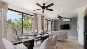 A modern dining area with a glass table, grey chairs, and ceiling fans. - 2 BD w/ Balcony and Rooftop Pool (Tulum)