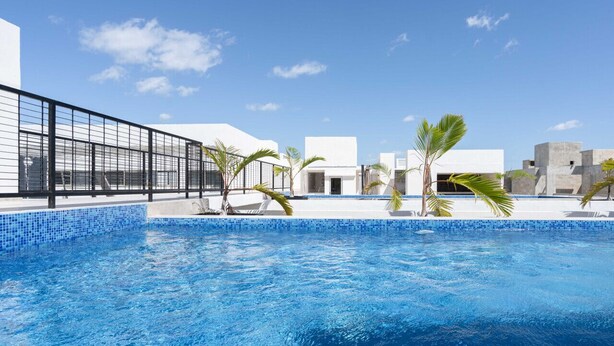 A swimming pool with clear blue water, surrounded by white buildings and palm trees. - 2 BD w/ Balcony and Rooftop Pool (Tulum)