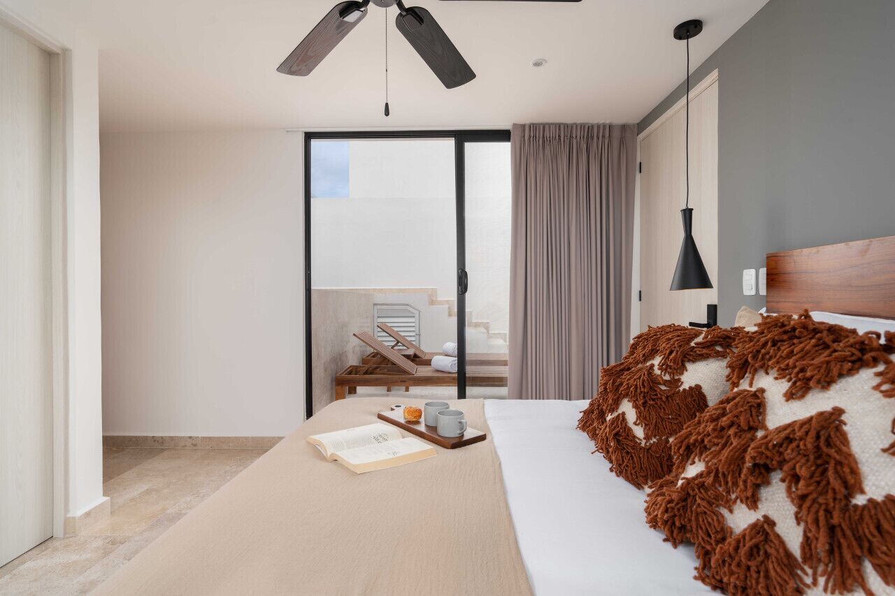Ein modernes Hotelzimmer mit einem Bett, einer Leseecke, einem Balkon mit Stuhl und einem Deckenventilator.