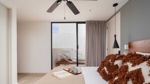 A modern hotel room with a bed, a reading area, a balcony with a chair, and a ceiling fan. - Penthouse Suite with Private Plunge Pool (Tulum)