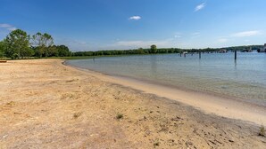 A sandy beach with clear water, trees, and a dock.