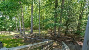 A wooden bridge leading into a forested area with a wooden fence and a bench.