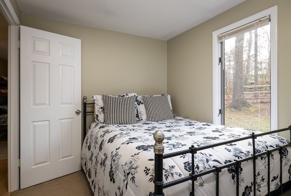 A bedroom with a bed, a door, and a window with a view of trees.